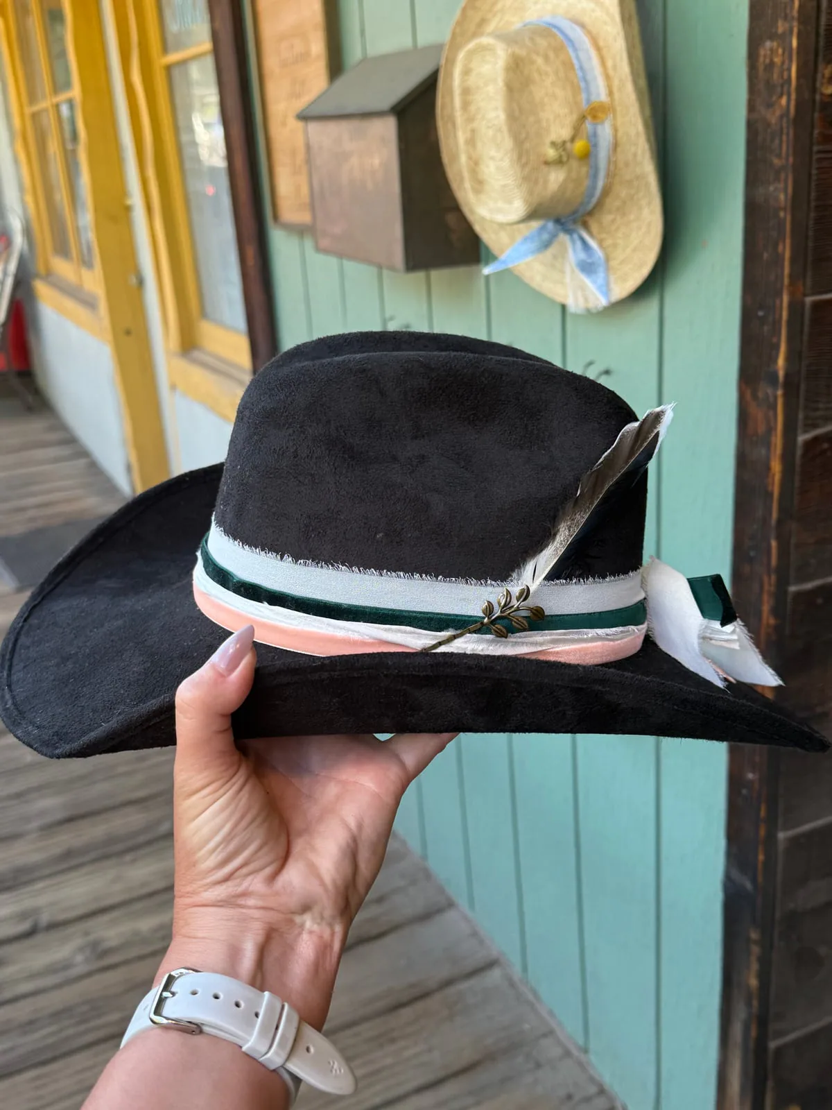 A darker western look with a soft ribbon finish. Black custom western hat with a pale ribbon band held in front of the hat bar trailer