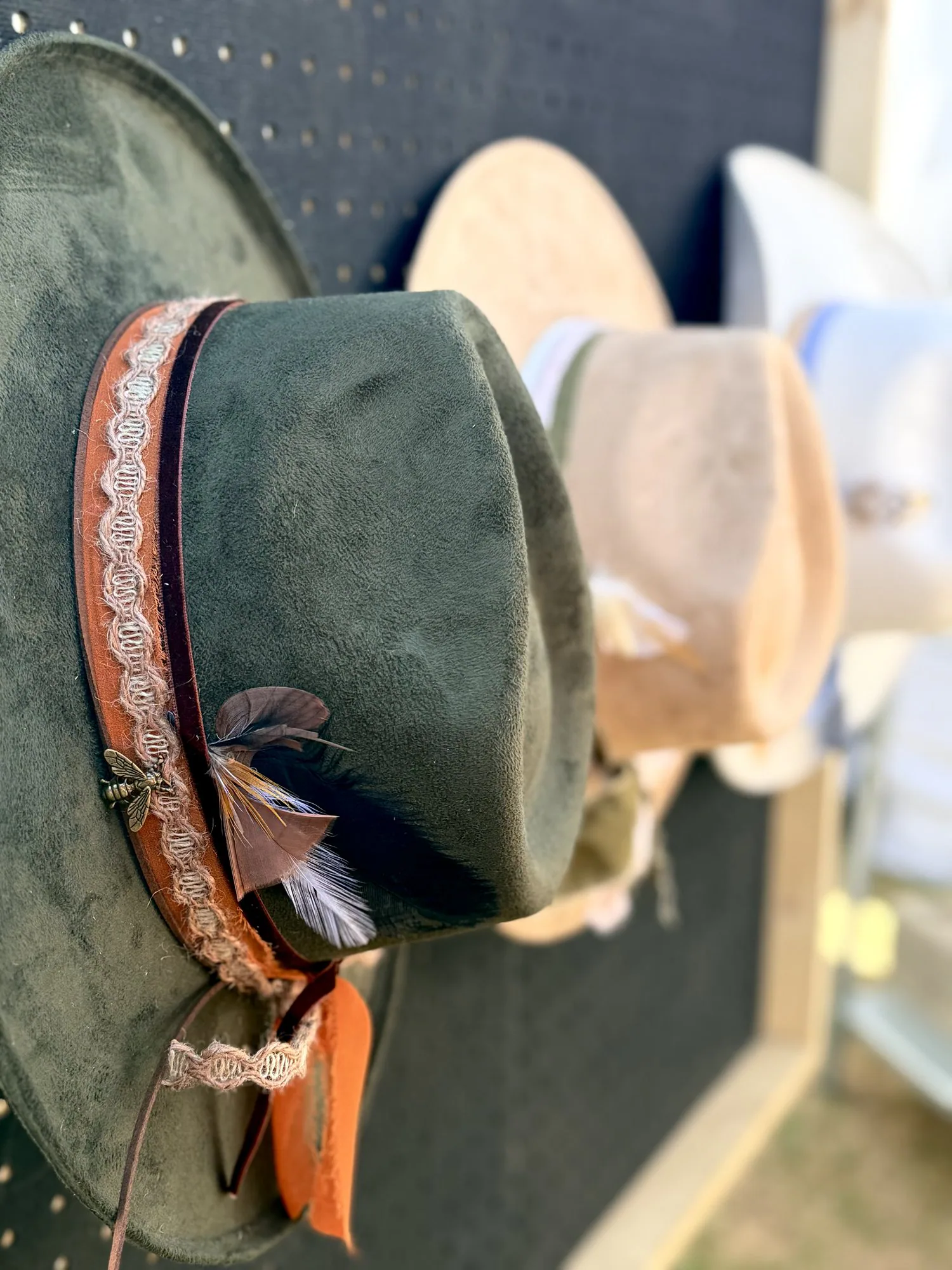 A look at the hat-bar details guests can make their own. Three custom western hats displayed on a wall with bands, feathers, and colorful trim