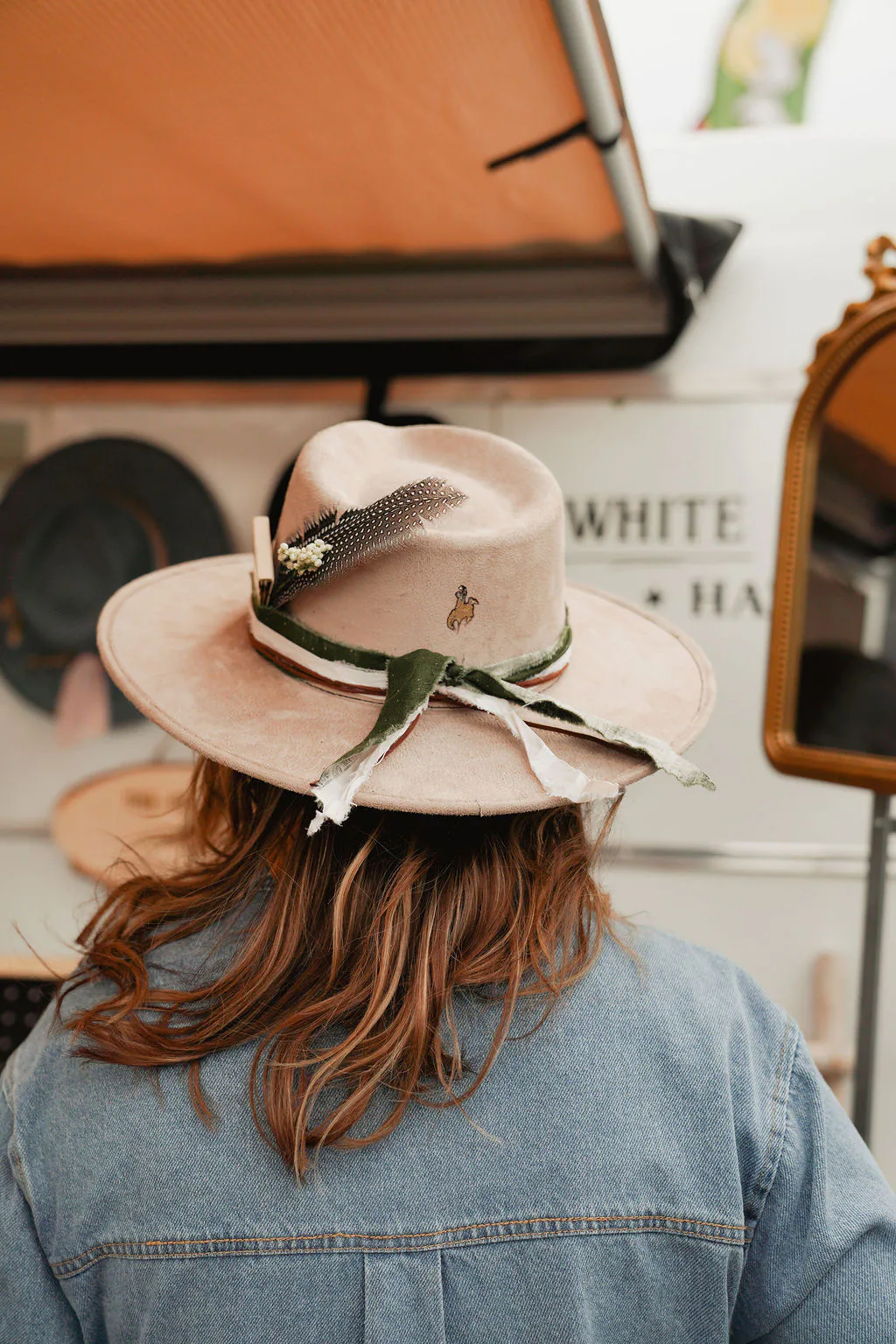 A one-of-a-kind hat to take home from the day. Finished cream western hat with ribbon and feather details worn in front of the White Rabbit display