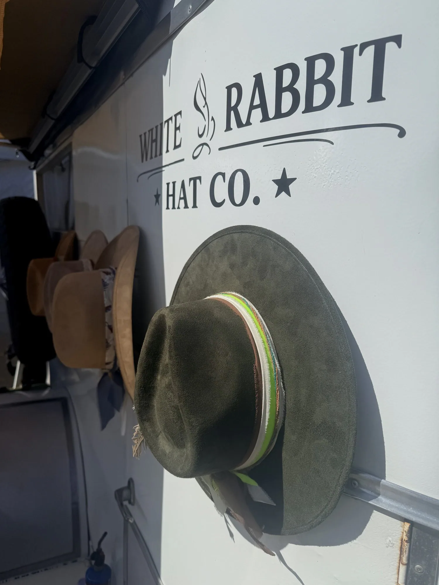 The White Rabbit Hat Co. setup brings the onsite hat-bar experience to Black Hat. White Rabbit Hat Co. trailer wall with a green western hat hanging below the logo