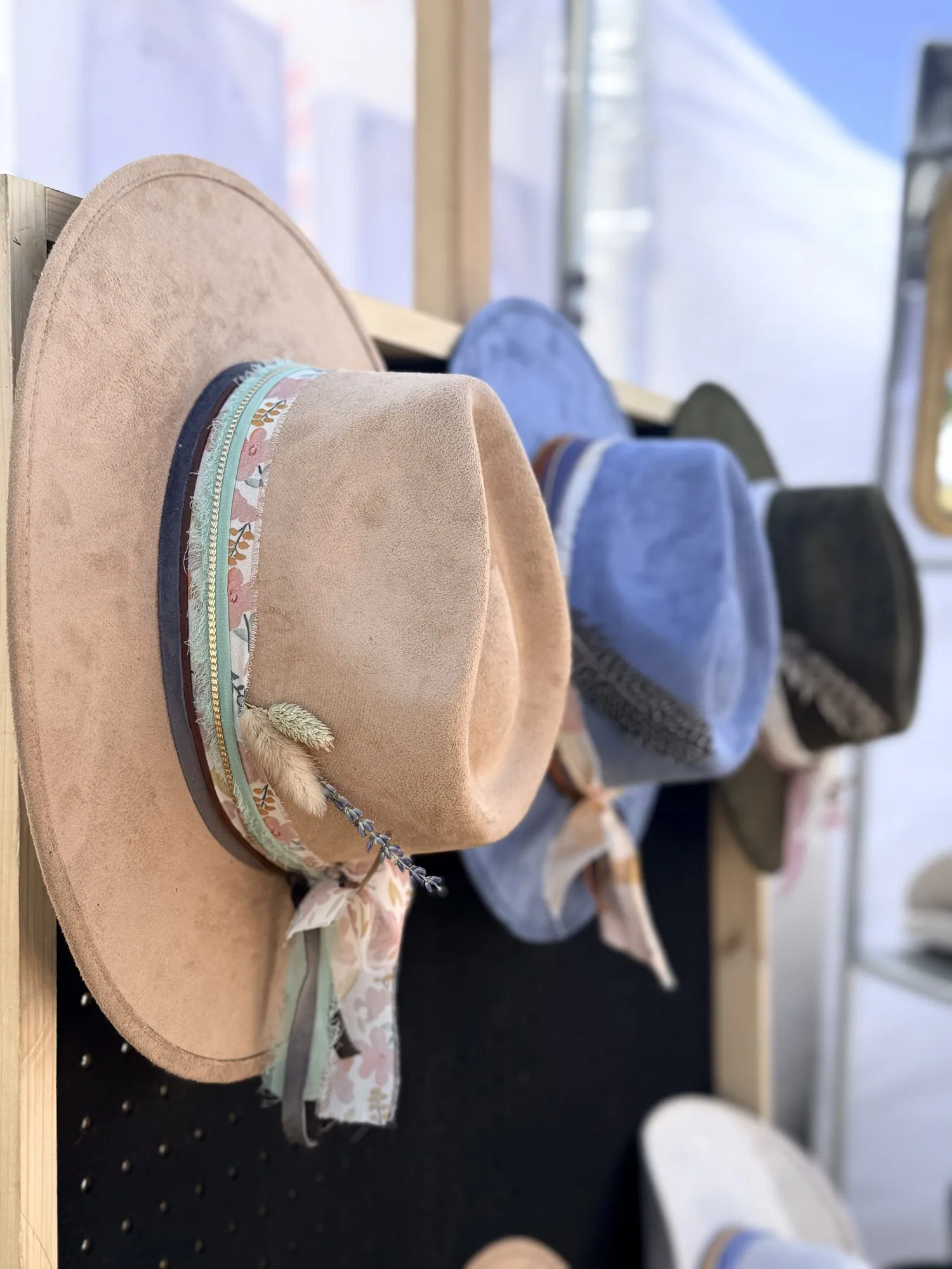 Choose your color, your band, and your finishing details. Neutral, blue, and blush western hats hanging on a display rack