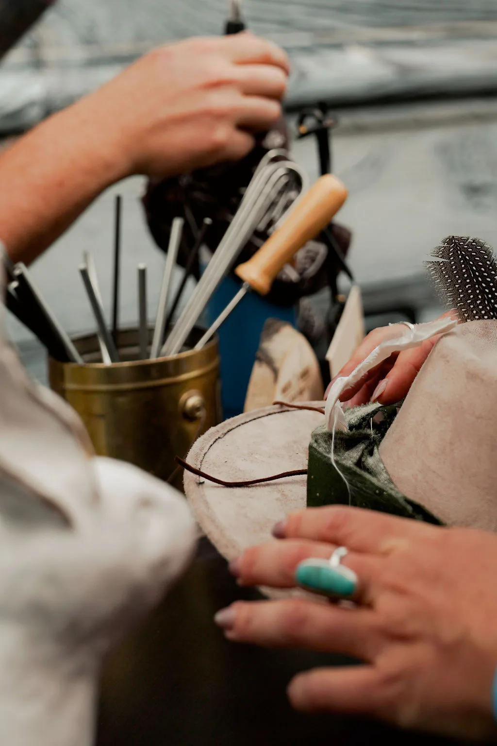 Hands-on trims, feathers, bands, and custom details. Hands choosing hat-bar trims, feathers, and styling tools for a custom western hat