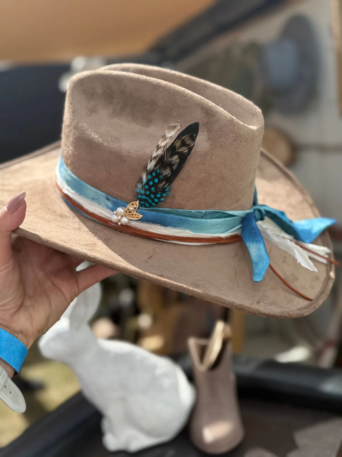 Color, trim, and feather choices create a one-of-a-kind finish. Cream western hat with a turquoise ribbon band and feather detail